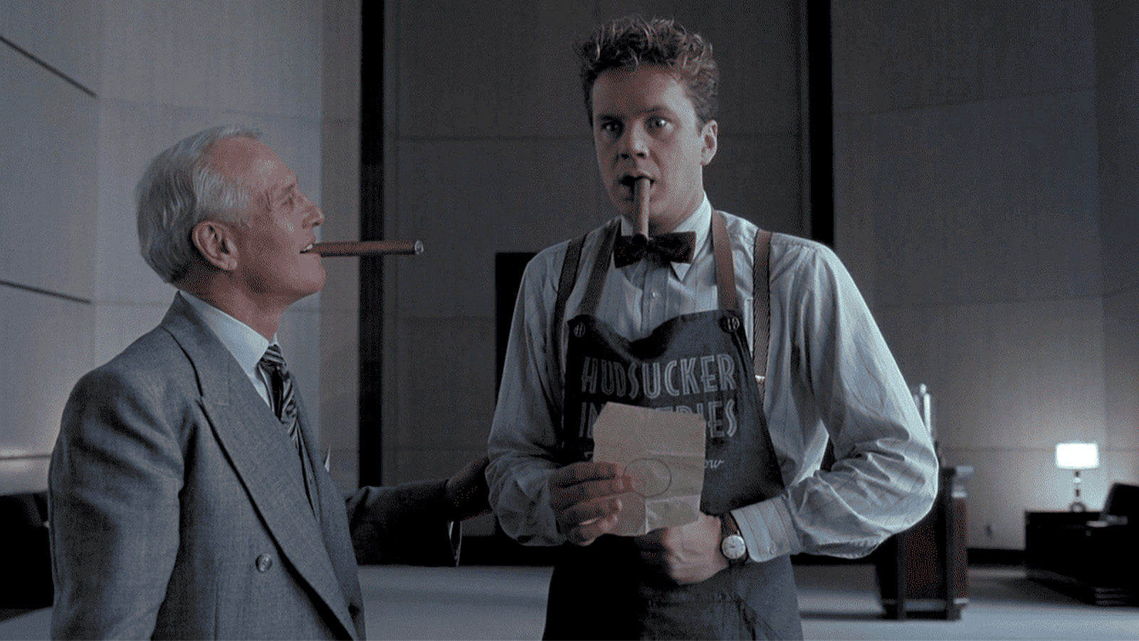 Paul Newman and Tim Robbins smoking cigars in a sparse gray office in a scene from The Hudsucker Proxy
