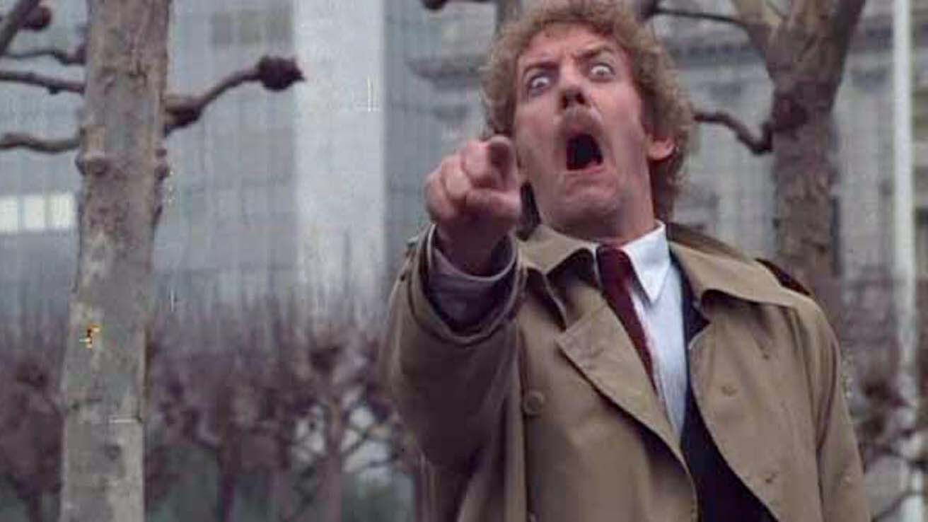 Donald Sutherland as Matthew Bennell, mouth agape, pointing toward the camera, in a scene from Invasion of the Body Snatchers