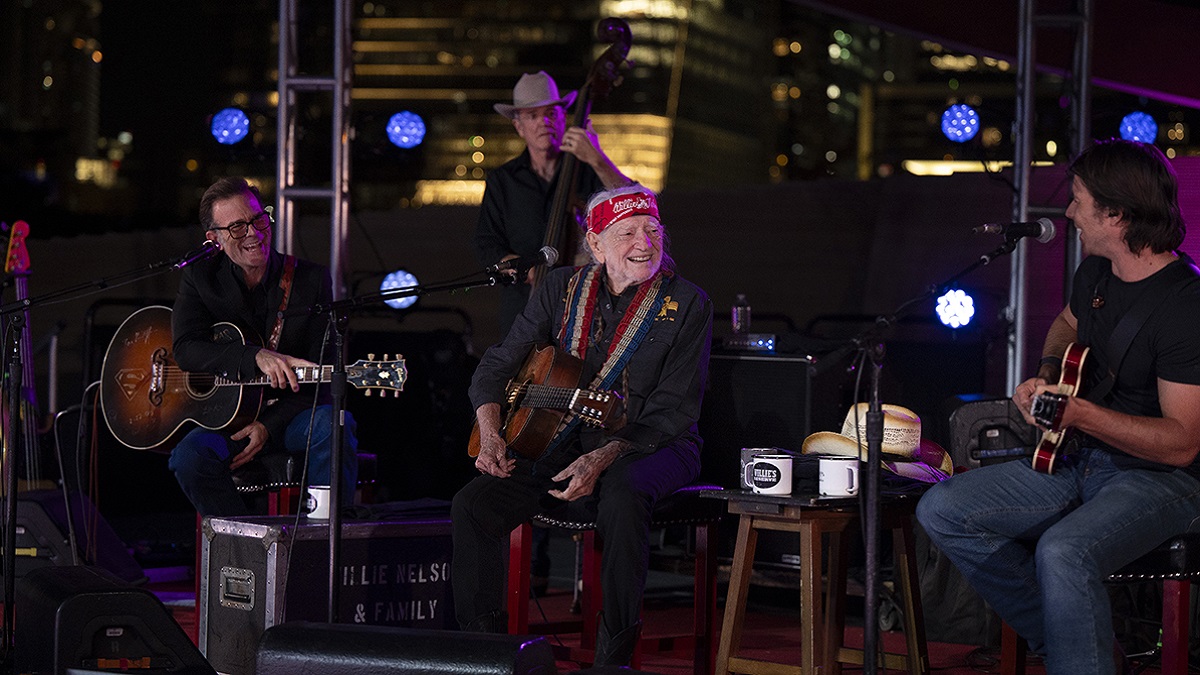 Willie Nelson sitting on stage with others
