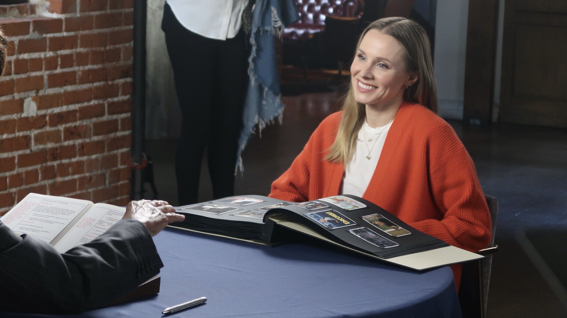 Kristen Bell sits with her open Book of Life, on a blue table