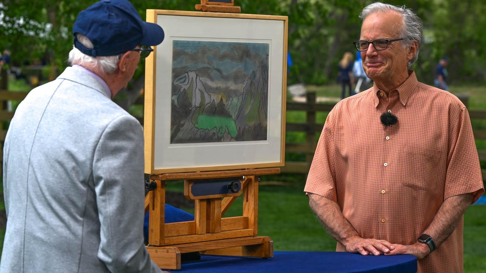 Two people, one with their back to the camera, stand on either side of a painting displayed on an easel