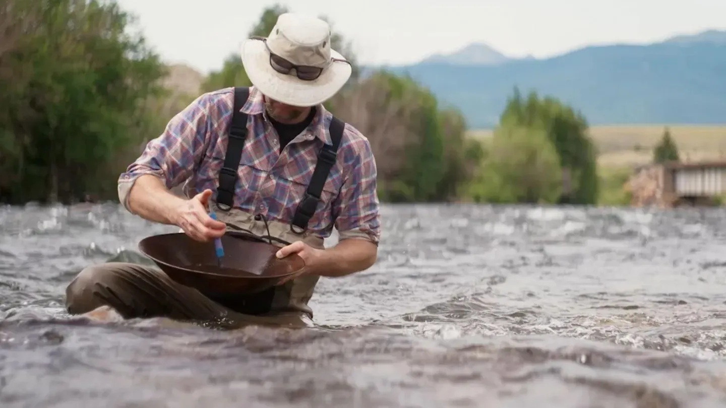 A person in waders in a river panning for gold