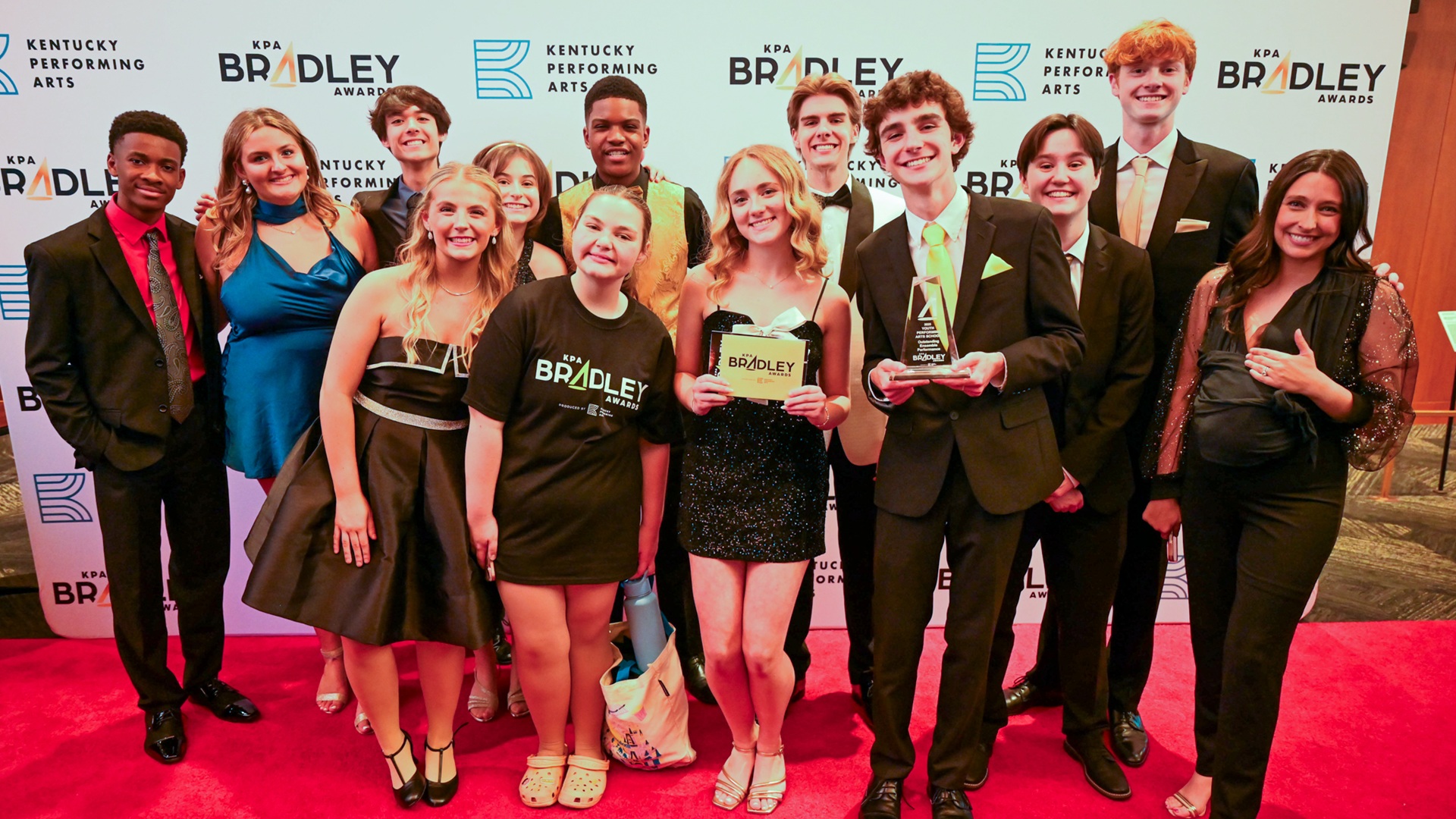 Group of students and teacher with award in front of a backdrop on a red carpet