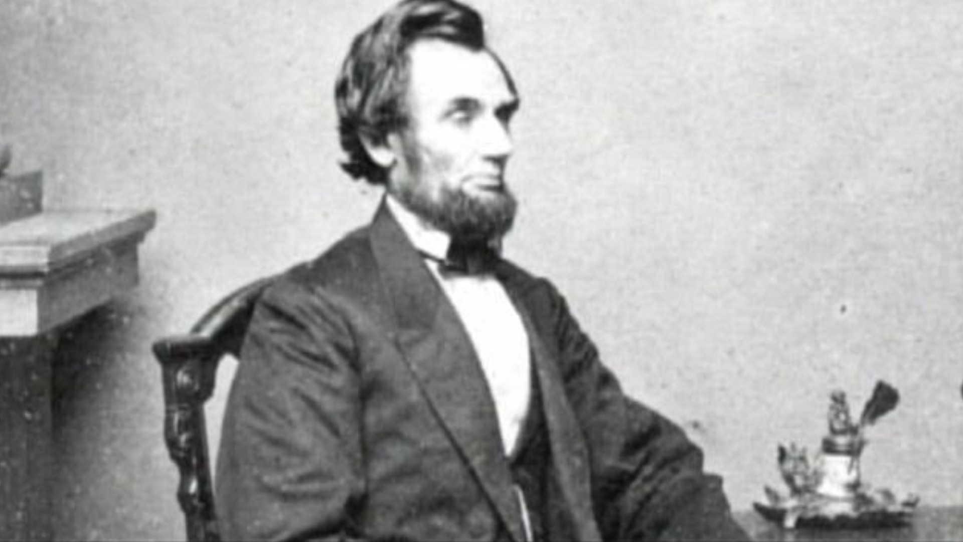 A photograph of Abraham Lincoln seated next to a table