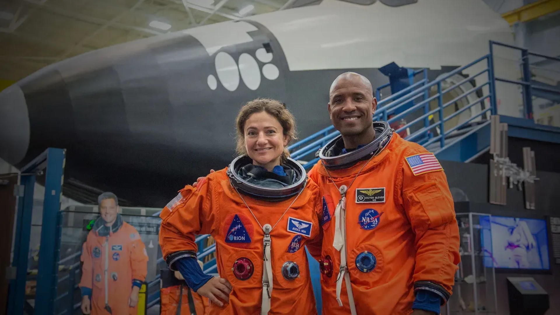 Two NASA astronauts posed and smiling in orange space suits.