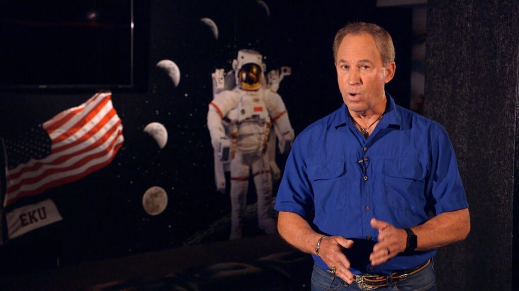 Kentucky Life host Doug Flynn in front of a picture of a space suit and pahses of the moon
