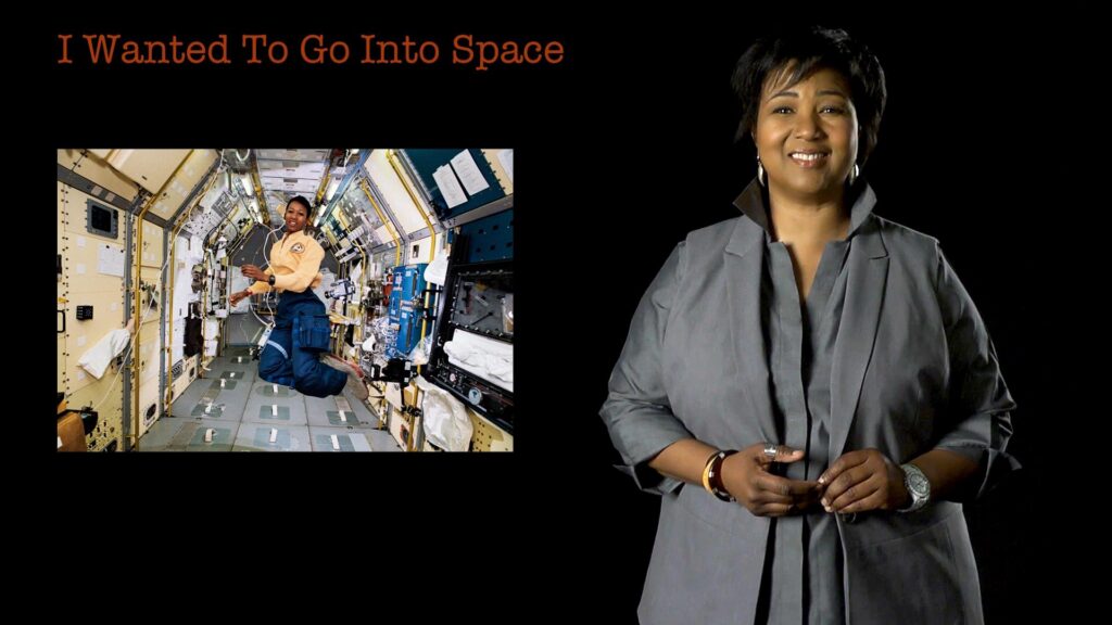 Mae Jemison standing beside a picture of herself on on a space ship and