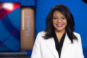 Host Renee Shaw smiling in a white jacket and black blouse with a KET set behind her.