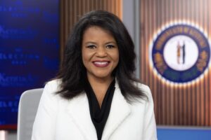 Host Renee Shaw smiling in a white jacket and black blouse with a KET set behind her.