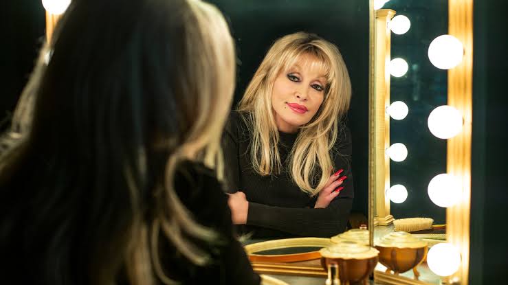 Dolly looking into a mirror with light bulbs around the edges