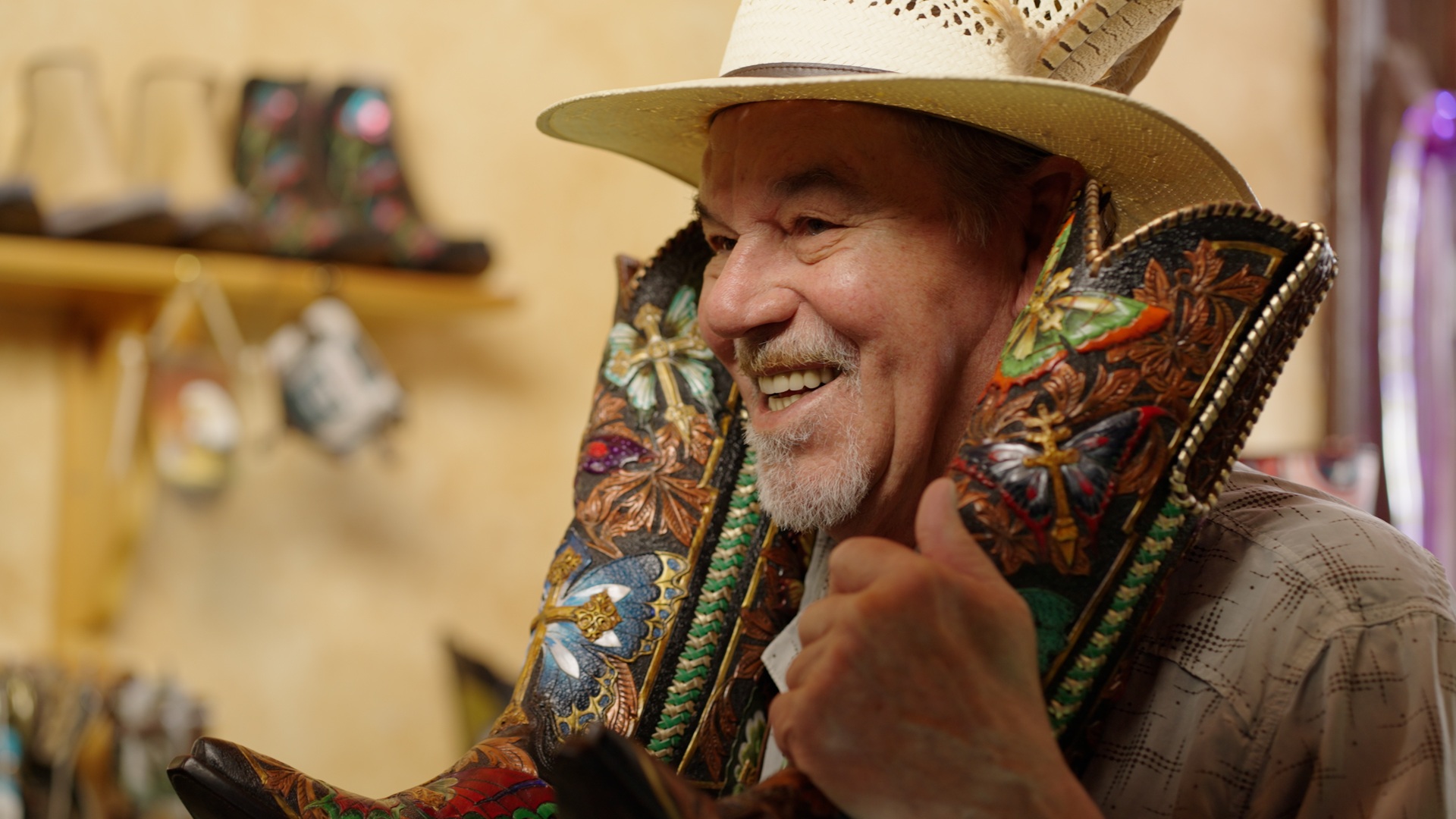 Person wearing a hat and holding up decorated cowboy boots by their face