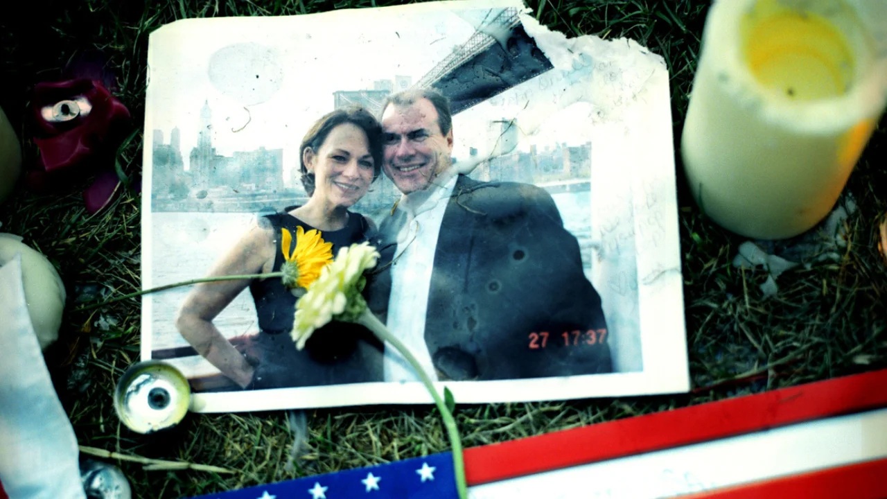 Photo of John O'Neill and wife among candles and flowers at a memorial