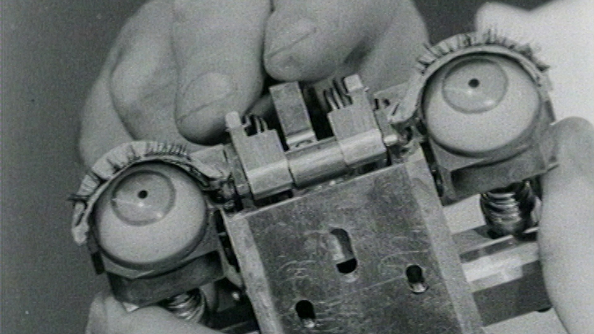 Black and white photo of a hand holding a machine that has human-like eyes