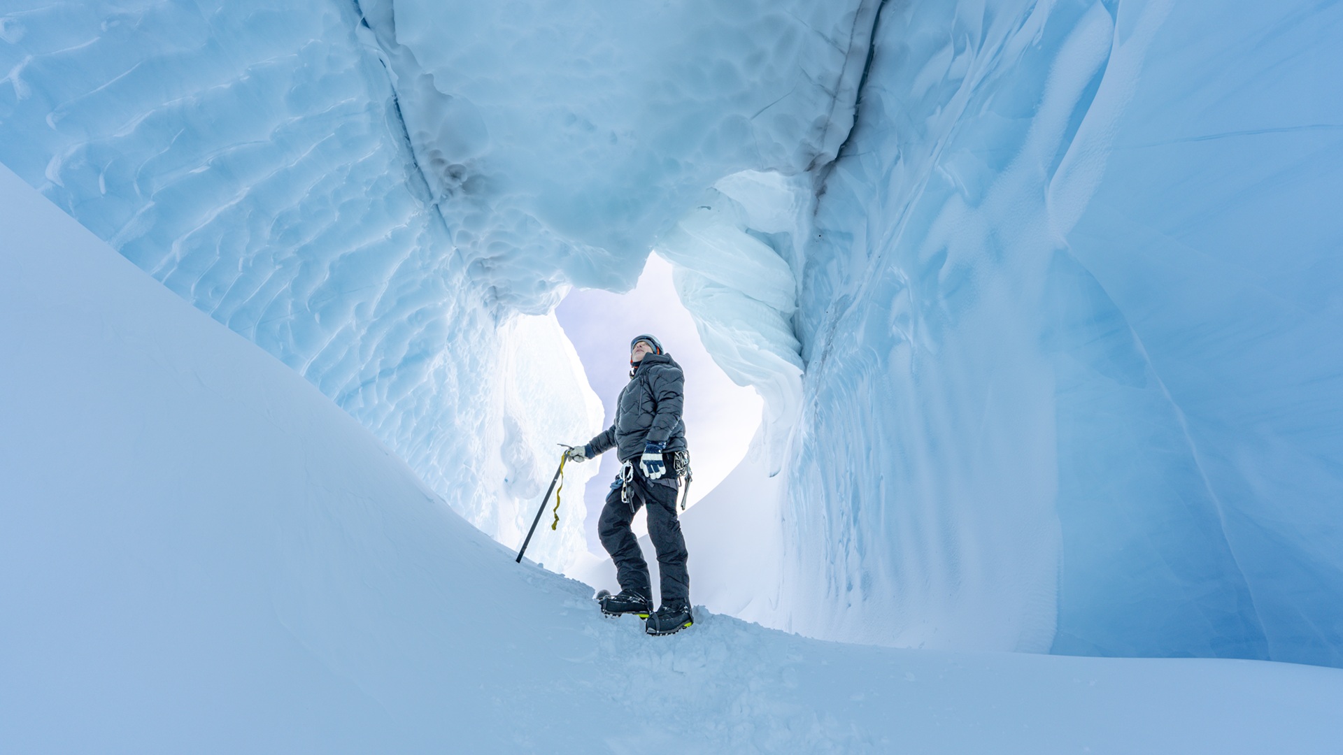 Professor Alun Hubbard dressed in winter hiking gear stands in opening of an ice cave