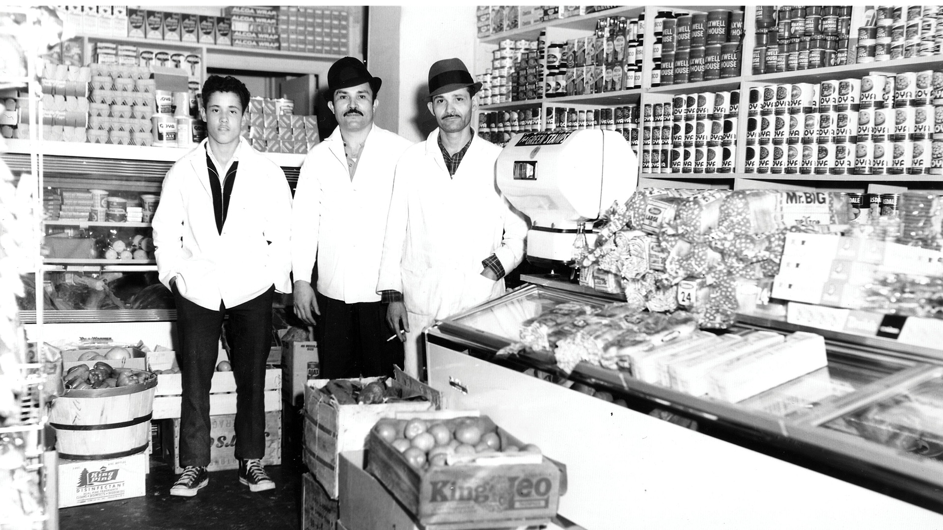 black and white photo of three people posing in a new york grocery store/bodega around 1960s