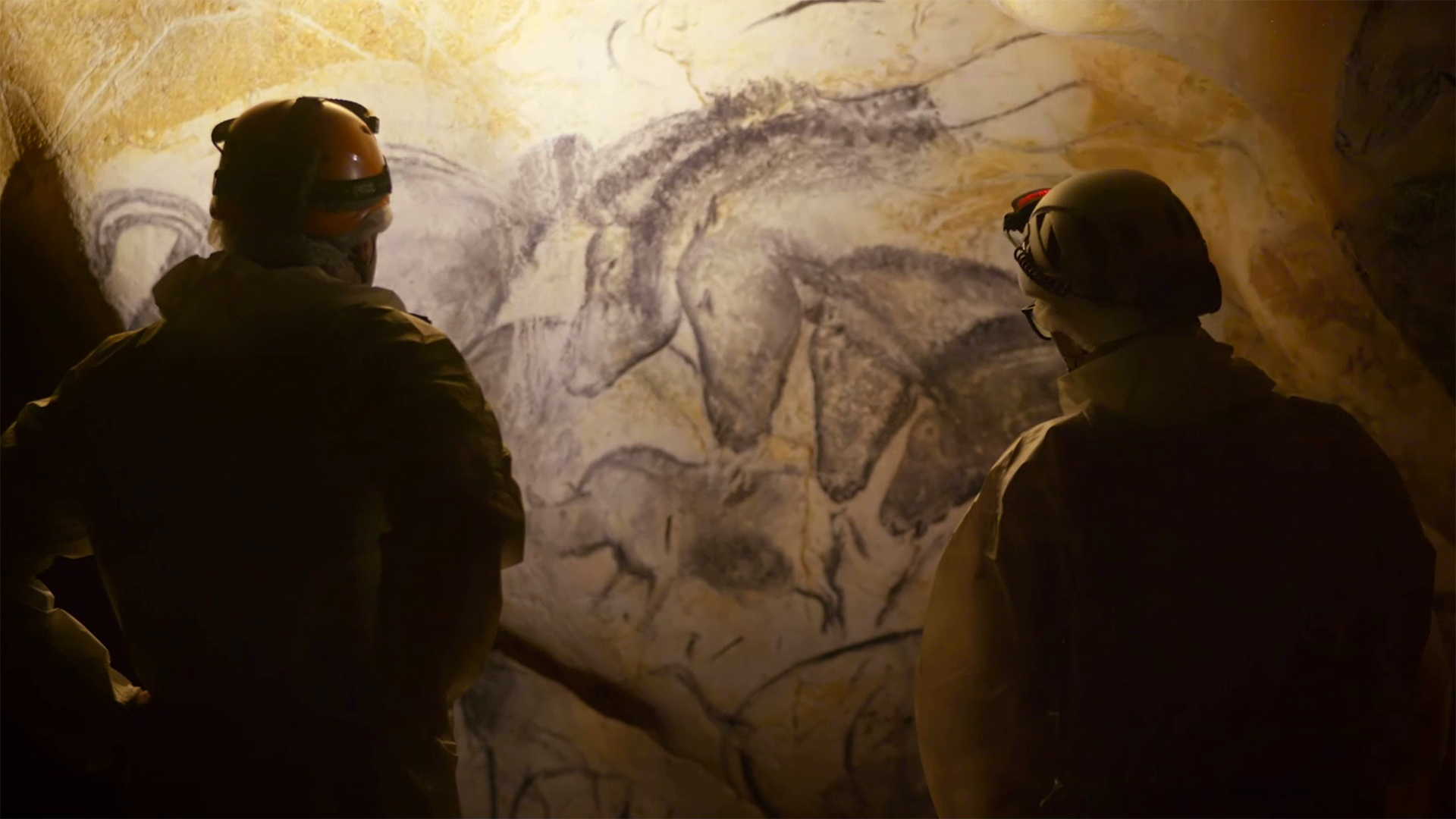 Two people in silhouette looking at a cave painting