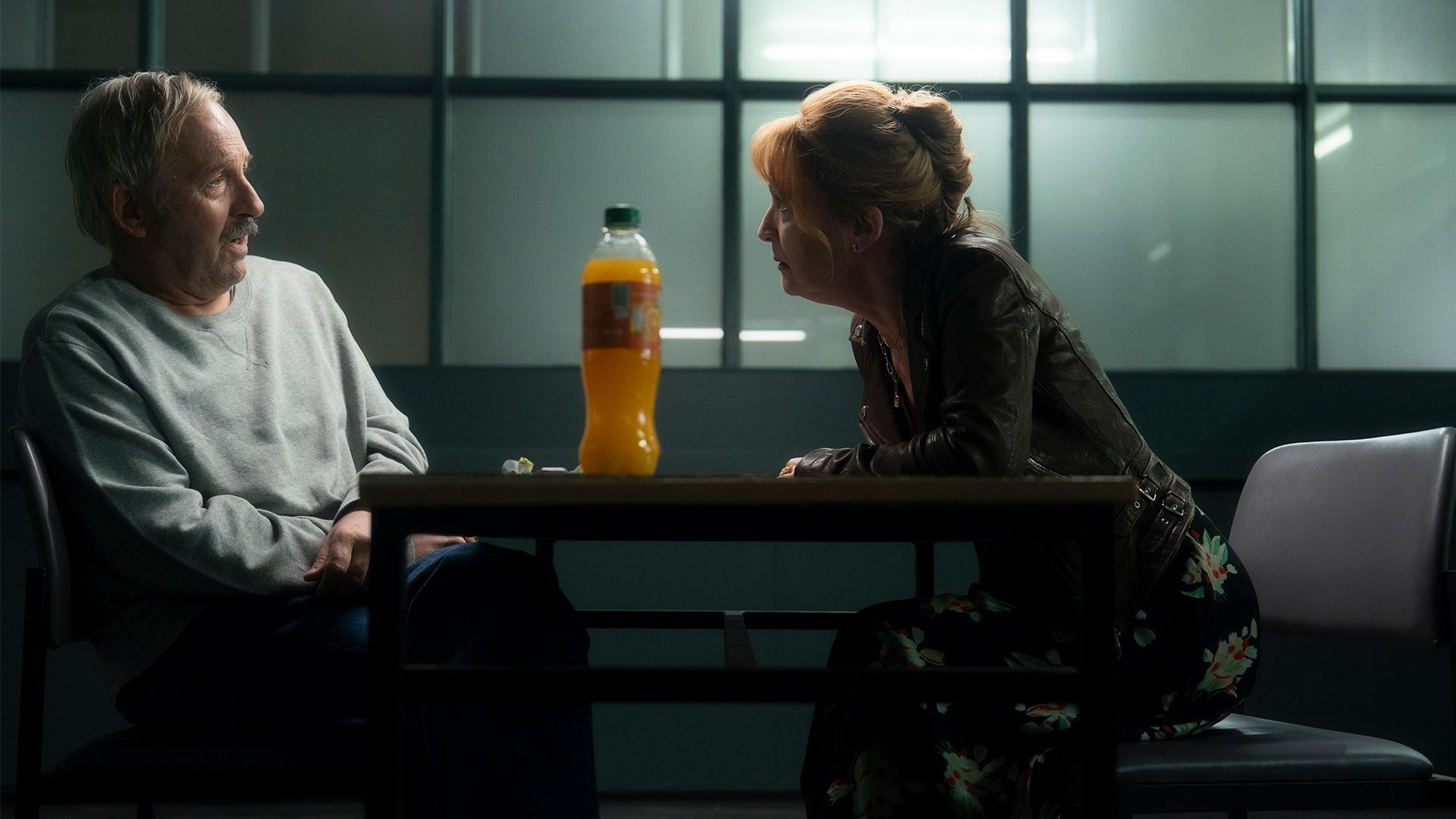 Susan leans across a table, a suspect on the other side