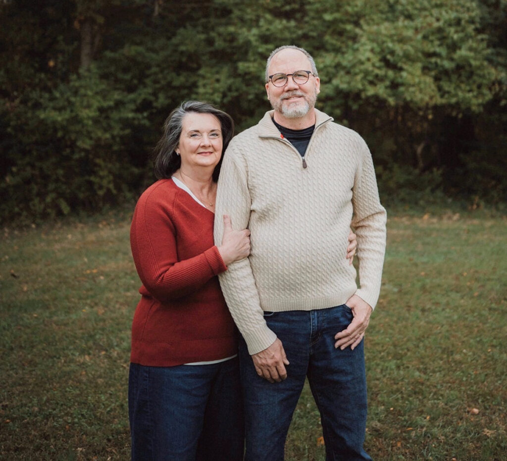 Tom and Kim Banta standing together outside with trees and bushes in the background