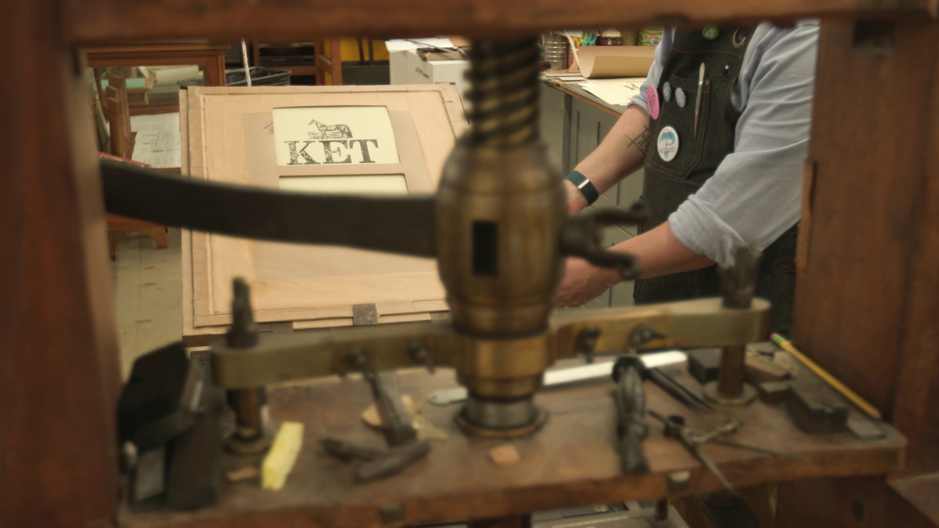 View through an antique printing press as a person's hands operate it and print a paper with a horse and KET