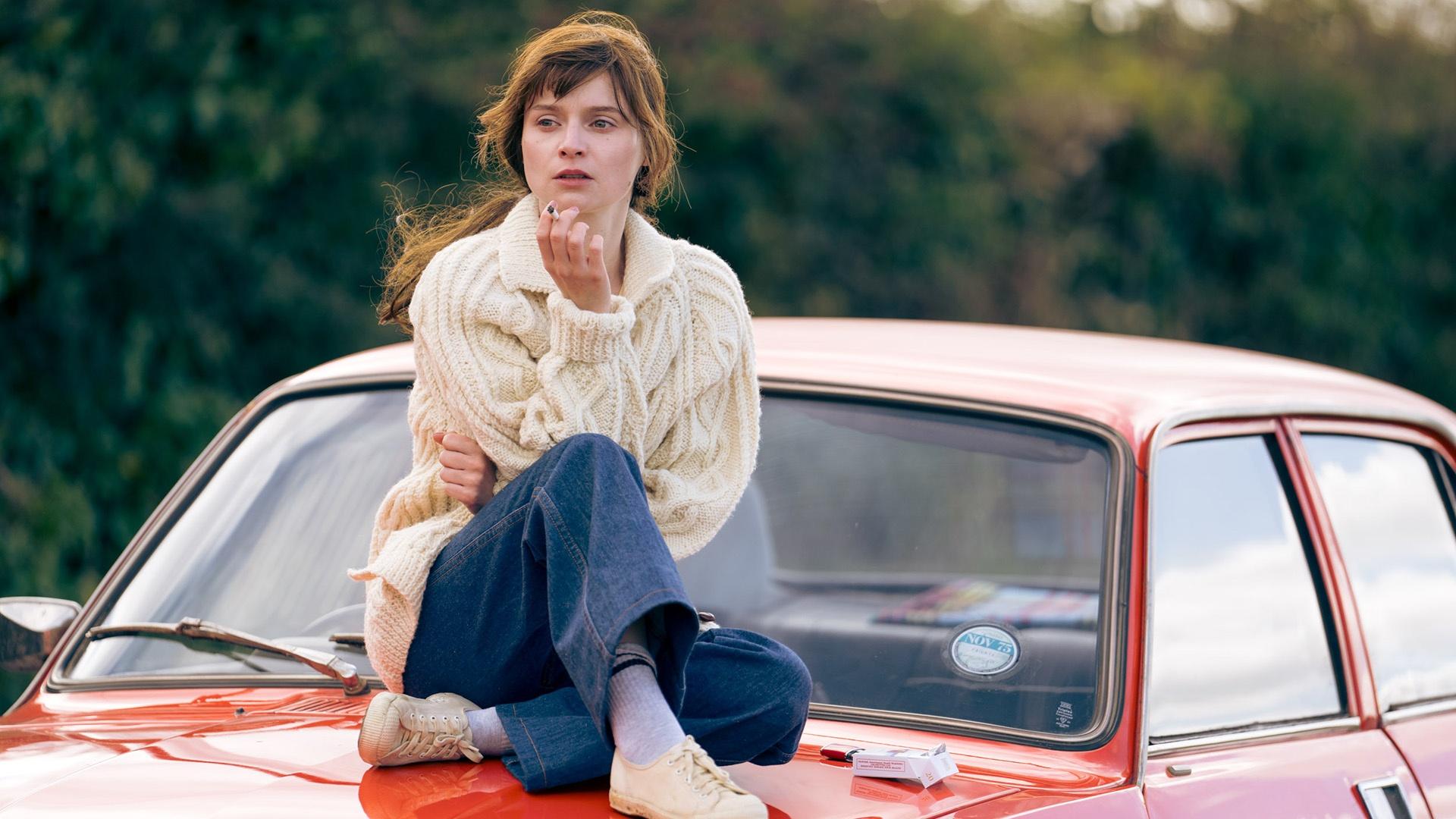 Cushla sits on the hood of a red car