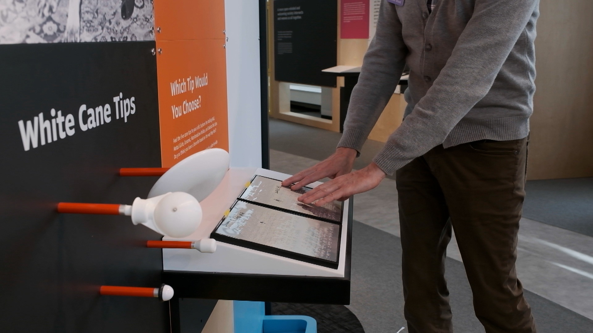 Person exploring an exhibit through braille next to some examples of tips for white canes