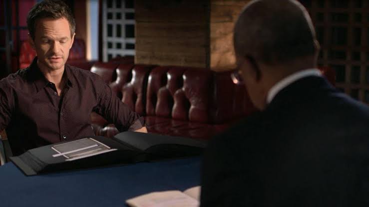 Neil Patrick Harris sits across from Henry Louis Gates, Jr., looking down at his Book of Life