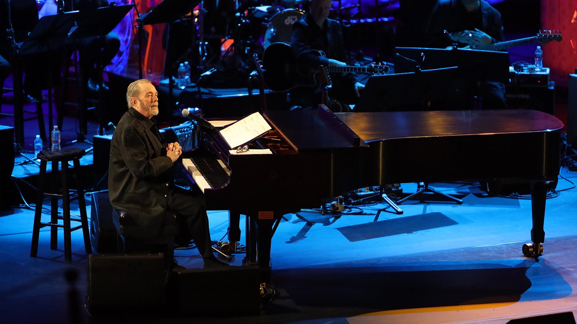 Jimmy Webb on stage at a piano, an orchestra behind him