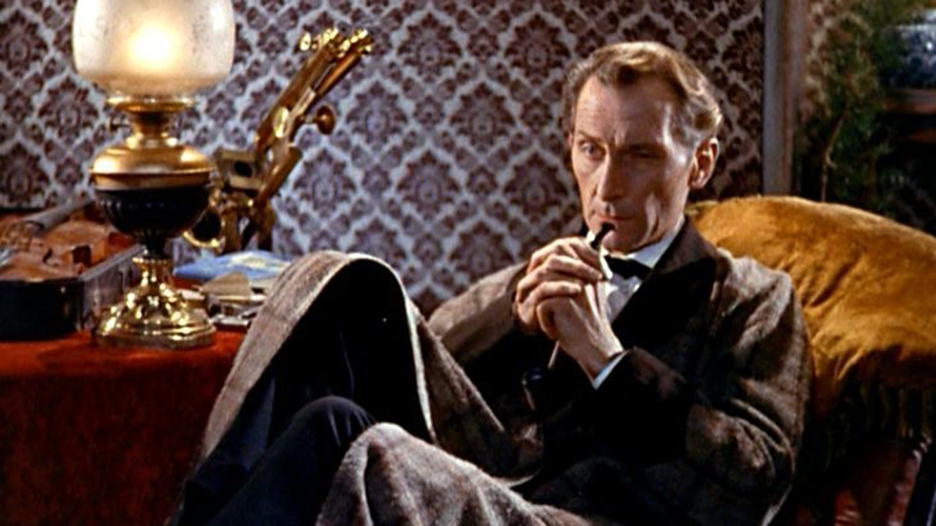 Peter Cushing as Sherlock Holmes sitting in a chair with his pipe, a lamp on a table next to him